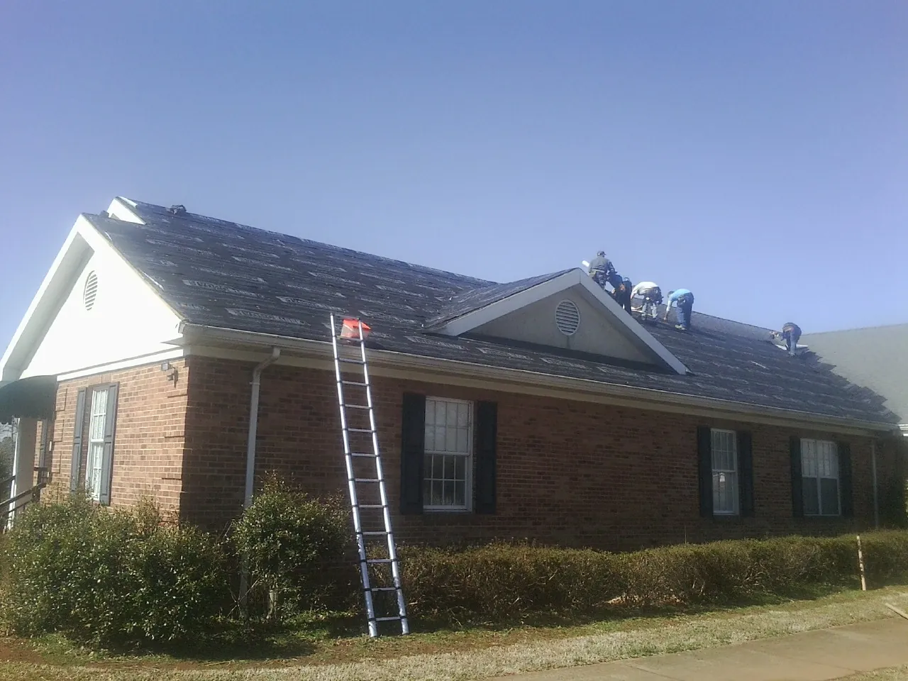 Crew tearing shingles off a brick ranch roof with a ladder set — Emergency Roof Repair work by our crew in Odessa